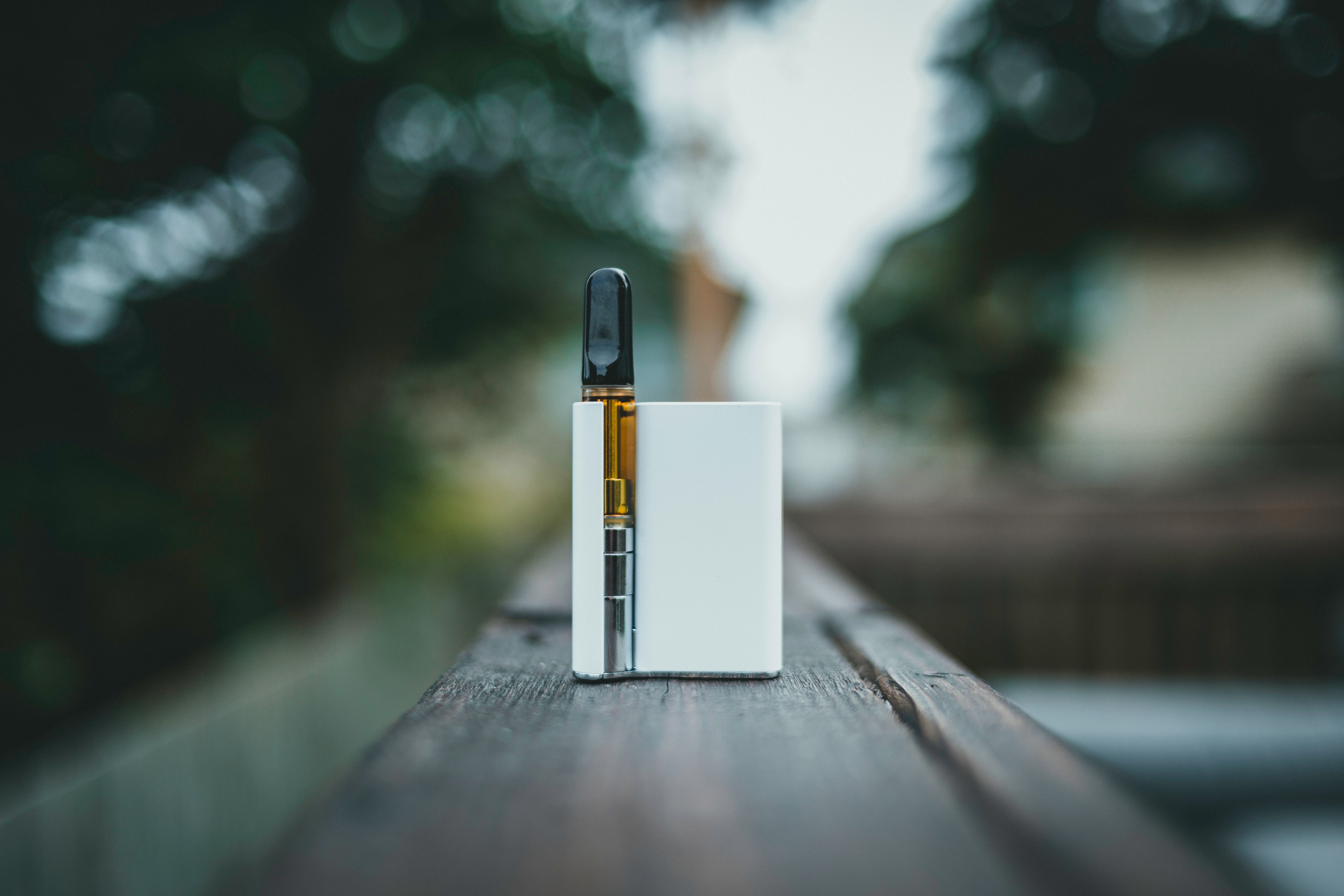 "A device used for vaping is shown on a wooden surface with a forest background"